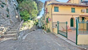 Una calle estrecha con muros de piedra a un lado y un edificio amarillo con una verja verde al otro.