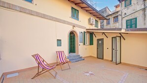 Un espacio exterior con dos sillas de playa a rayas, una puerta verde y un patio con baldosas.
