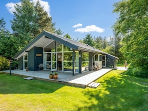 Une maison moderne dotée d’une grande façade vitrée, d’une terrasse et d’un jardin.