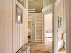 A hallway with wooden walls, a bench, a mirror, and a bed in the background.