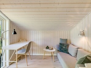 Une pièce confortable avec un bureau blanc, deux chaises, une petite table ronde, un canapé et une lampe fixée au mur.