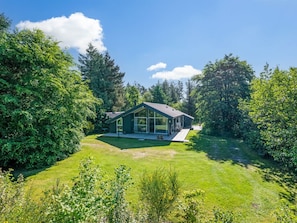 A modern house with a large glass window, surrounded by lush greenery and a clear sky.