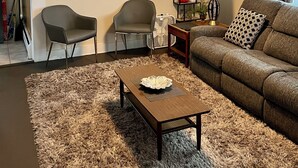 A living room with a sofa, two chairs, a coffee table, a painting, decorative wall accents, and a ceiling light.
