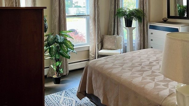 A bedroom with a bed, dresser, potted plants, and a window with curtains.