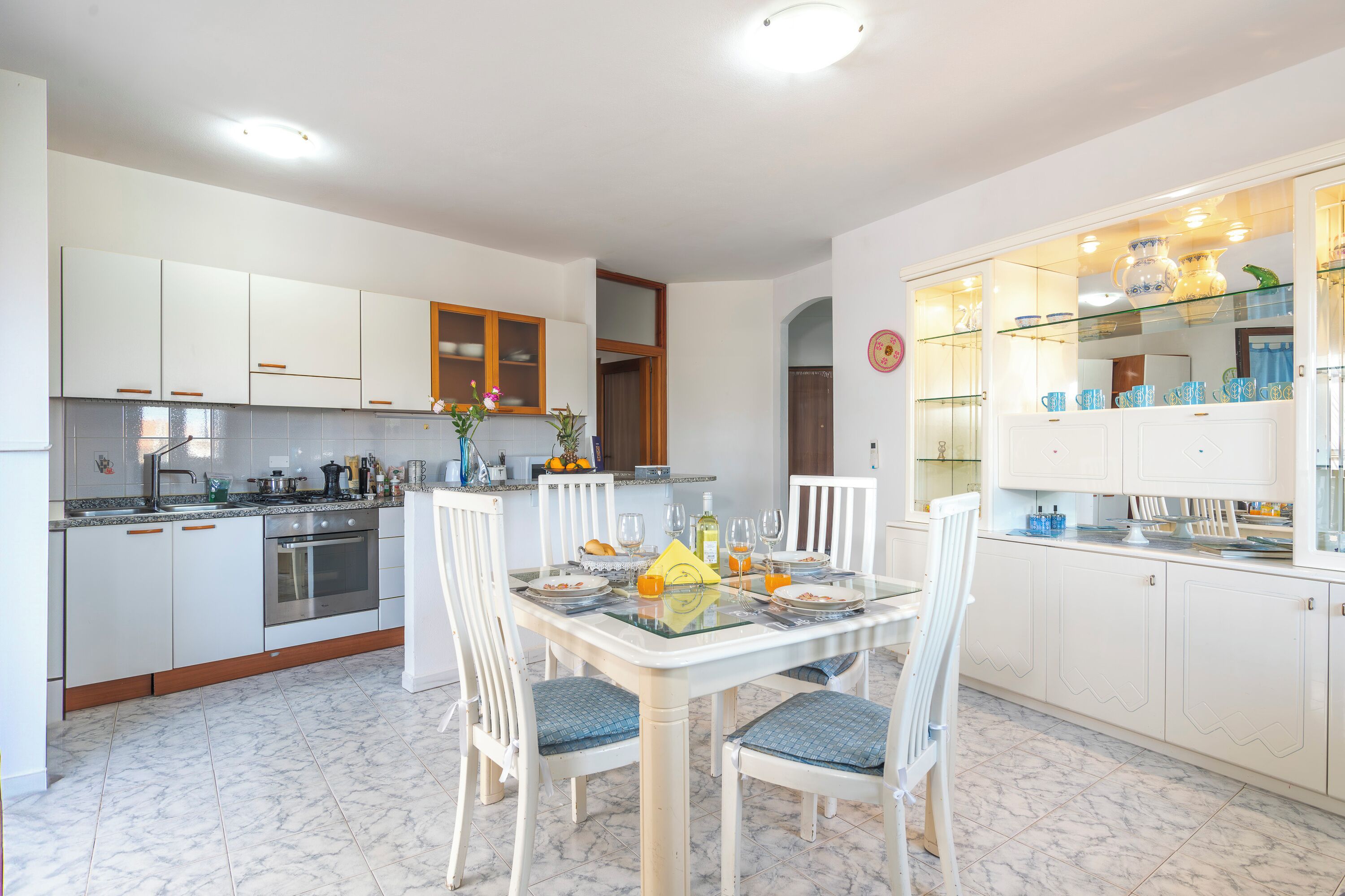 A modern kitchen with white cabinets, a built-in oven, and a dining area with a glass table and chairs.