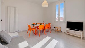 Ein modernes Wohnzimmer mit Essbereich, einem Fernseher auf einem Schrank und einem großen Fenster.