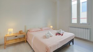 Ein Schlafzimmer mit einem Bett, Nachttischen, einer Lampe, einem Heizkörper und einem Fenster.