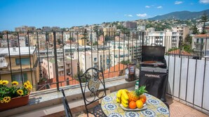 Un balcon avec un barbecue, une table avec des fruits et une plante en pot.