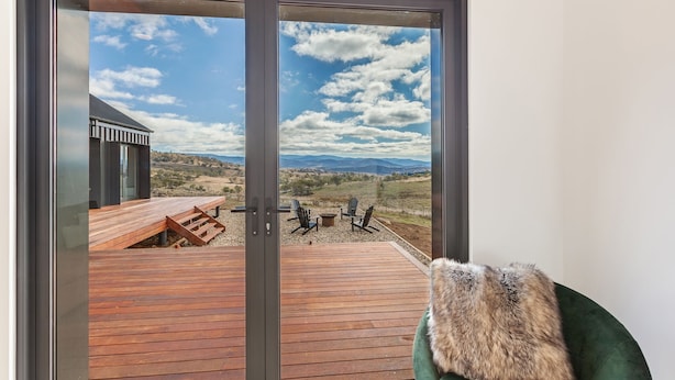 A modern outdoor deck with a wooden floor and a view of a mountainous landscape through a glass door. - Camber Farmhouse Jindabyne Countryside (Jindabyne)