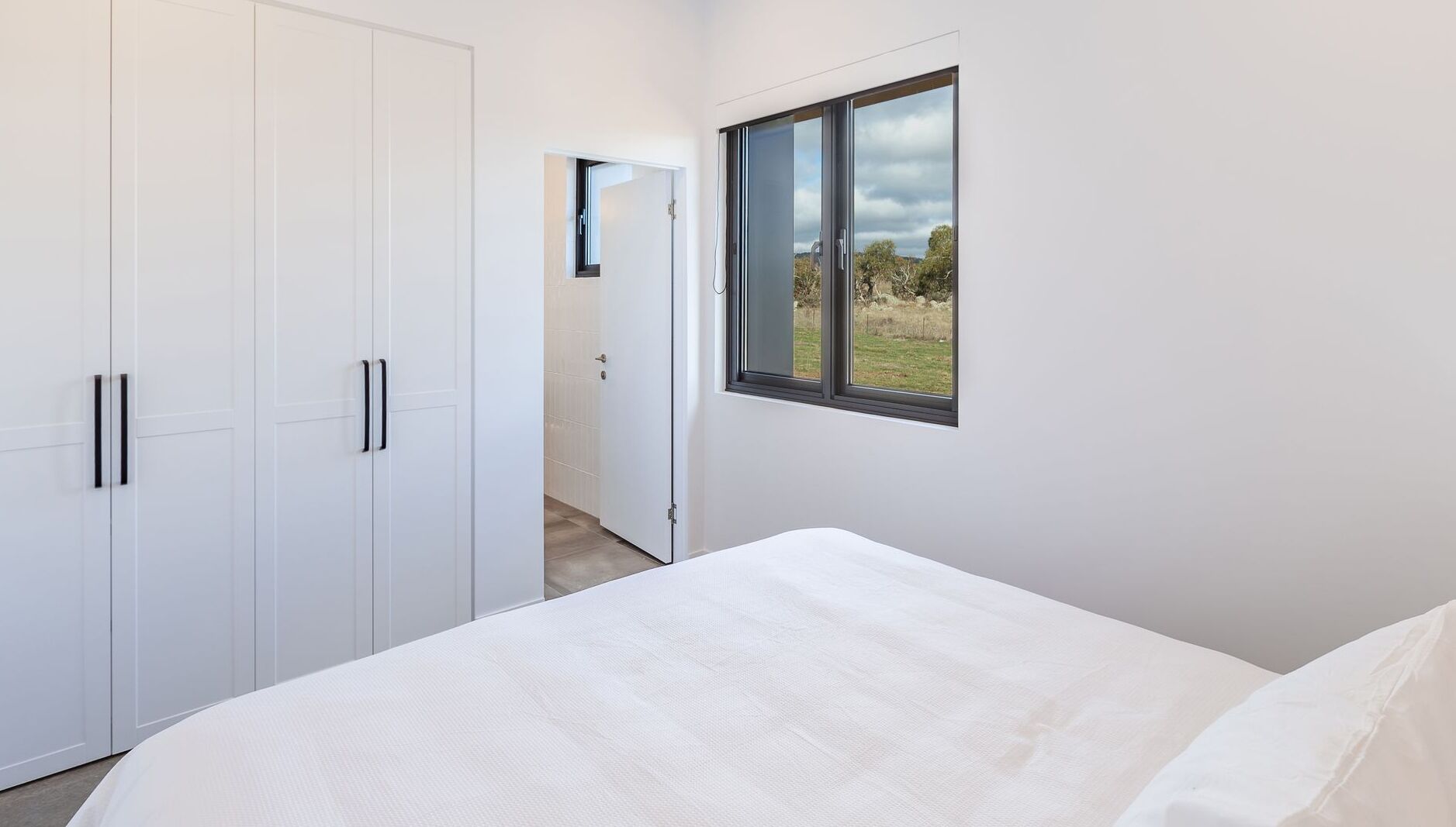 Une chambre avec un grand lit, une armoire blanche et une fenêtre donnant sur un champ verdoyant.