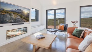 A modern living room with a fireplace, a large TV, and a sofa with cushions. - Camber Farmhouse Jindabyne Countryside (Jindabyne)
