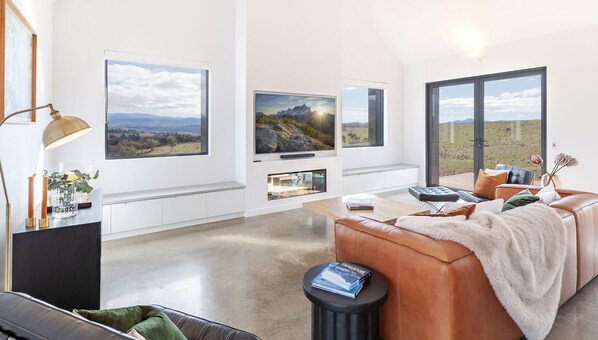 A modern living room with a large window, a flat-screen TV, a fireplace, and a leather sofa.