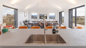A modern kitchen with a central island, a stainless steel sink, and a dining area with a view of the landscape. - Camber Farmhouse Jindabyne Countryside (Jindabyne)