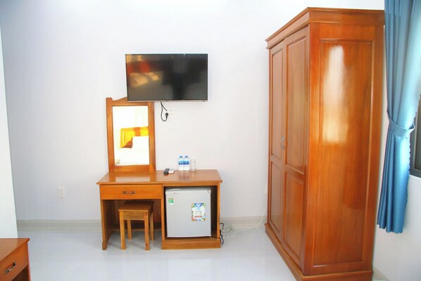 A room with a wooden desk, a small refrigerator, a television mounted on the wall, and a wardrobe.