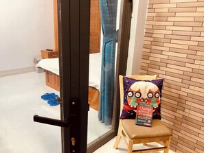 A room with a bed, a chair with a pillow, a book, and a door. - Huynh Han Hotel Can Tho by Bay Luxury (Can Tho)