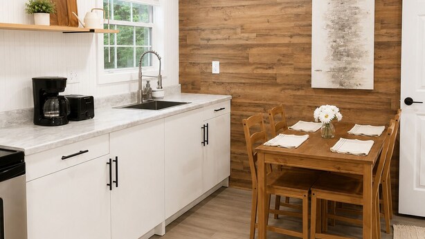 A modern kitchen with white cabinets, a wooden wall, and a dining area with a wooden table and chairs. - Private 1BR GuestHouse Near Charlotte Pet Friendly (Indian Trail)