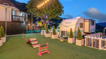 A backyard with artificial grass, a swing set, a playhouse, and a camper trailer.