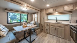 A compact RV kitchen with a dining area, a sink, and a stove.