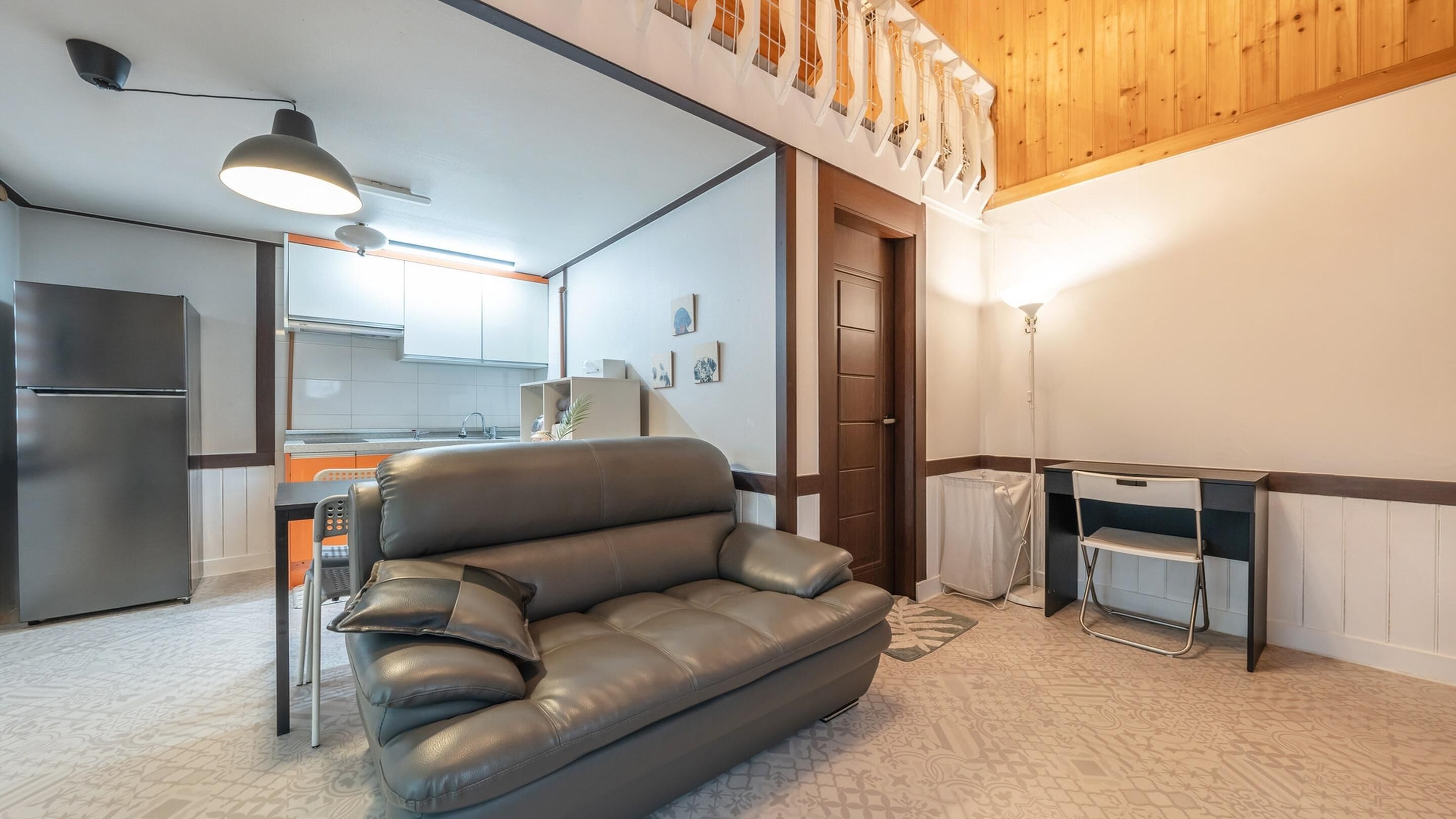 Una sala de estar moderna con un sofá de cuero, un comedor con mesa y sillas, una cocina con refrigerador, y un techo de madera.