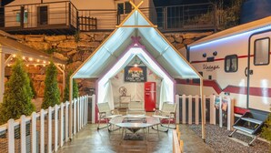A cozy outdoor seating area with a table and chairs, a red refrigerator, and a camper van parked nearby.