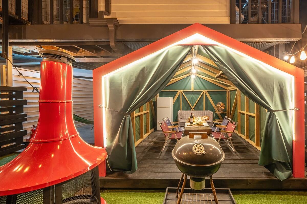 Un acogedor dormitorio en ático con techo inclinado, una cortina verde, una mesita con una botella y una parrilla.