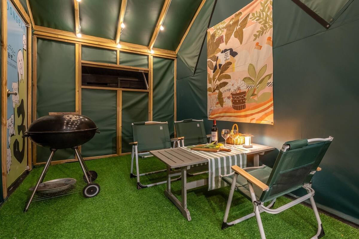 Una habitación con carpa, una mesa, sillas, una parrilla y un banderín decorativo.