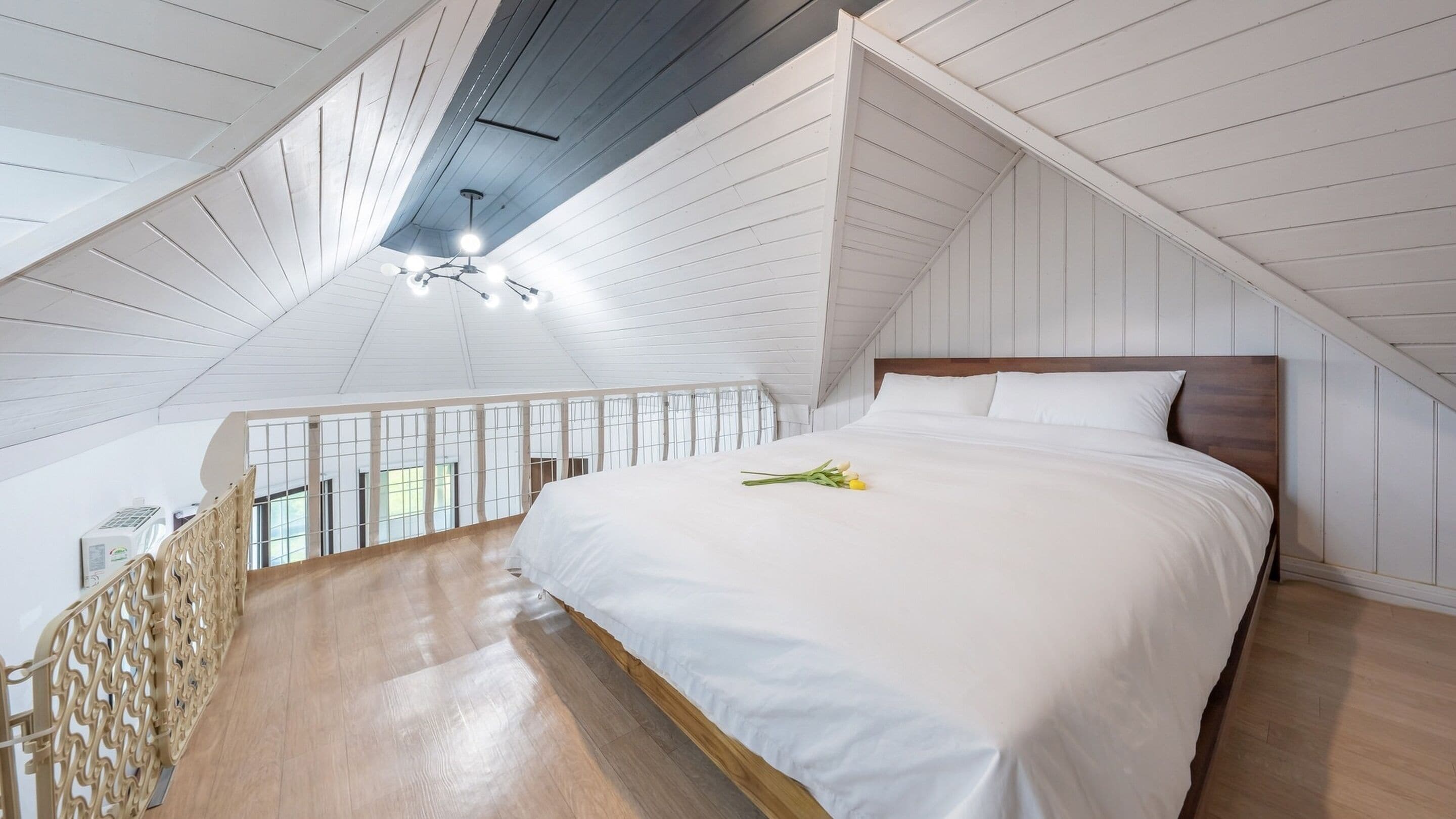 A bedroom with a wooden ceiling, a bed with white bedding, and a view of the outdoors through a balcony railing.