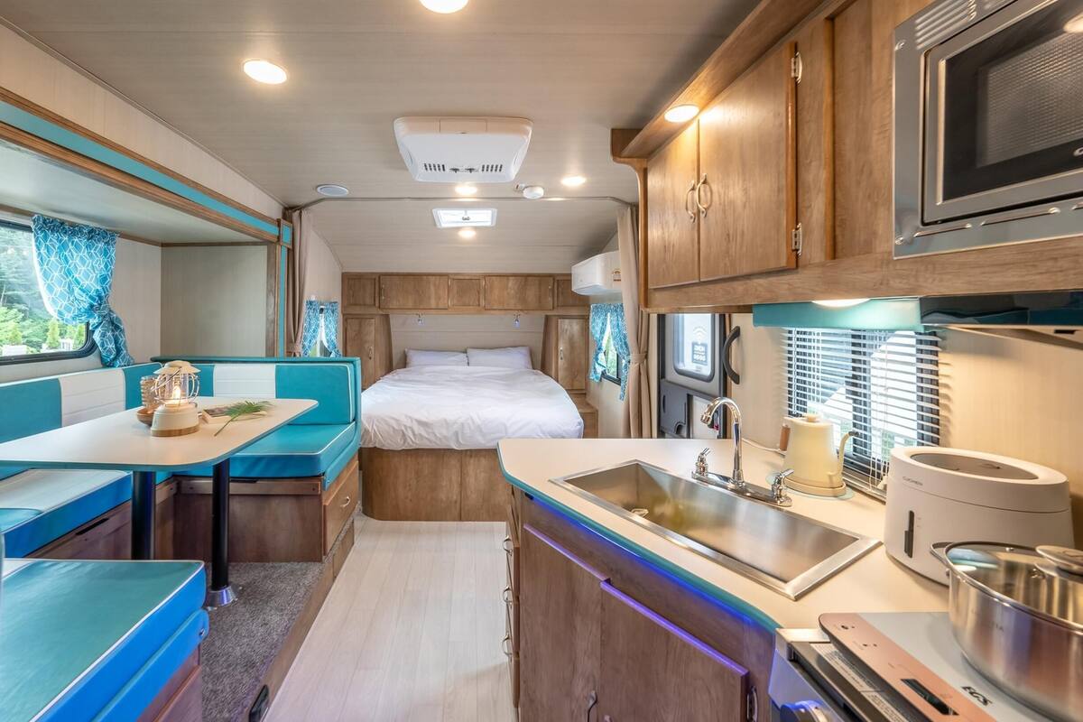 Interior compacto de una caravana con kitchenette, zona de comedor y litera.
