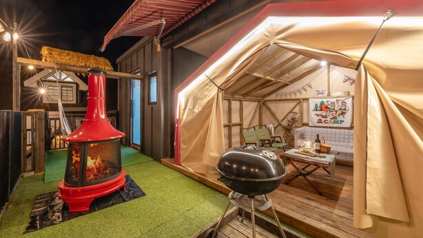 A tented outdoor area with a barbecue grill and a wood stove.