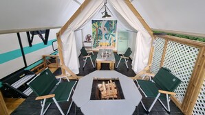 A tented room with a table and chairs, a painting on the wall, and a small refrigerator.