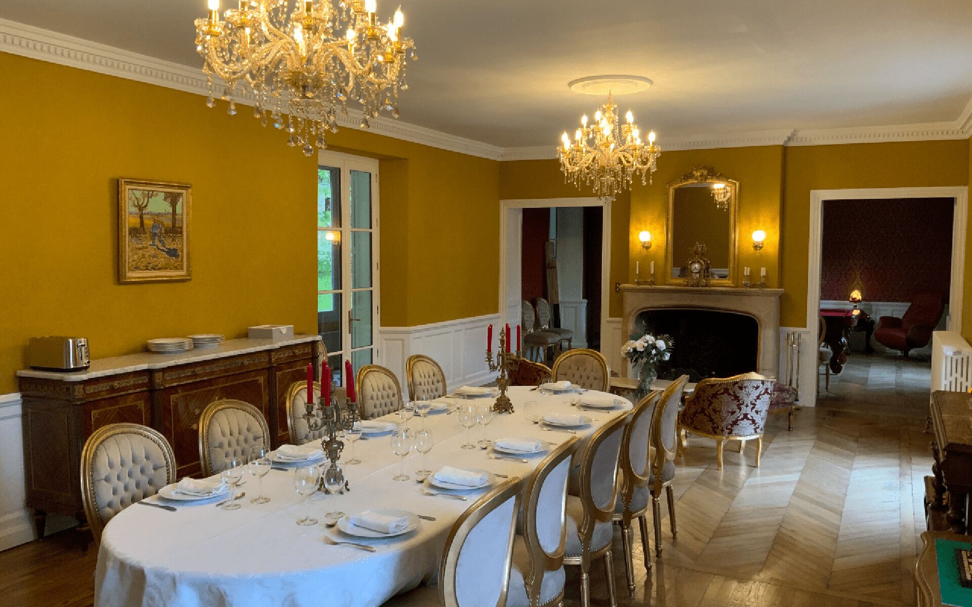 Une salle à manger élégante, avec une longue table dressée pour un repas, des lustres et une cheminée.