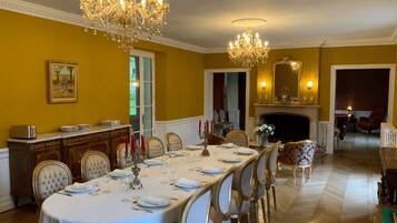 Une salle à manger élégante, avec une longue table dressée pour un repas, des lustres et une cheminée.