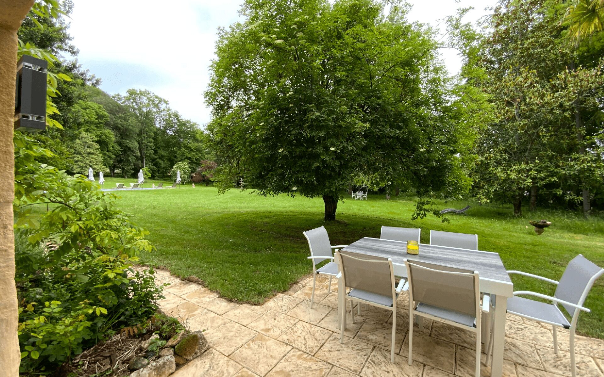 An outdoor patio with a table and chairs, surrounded by a well-maintained lawn and trees.