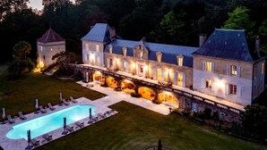 Una gran mansión iluminada con piscina y mobiliario exterior.
