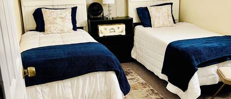 A hotel room with two beds, a nightstand, a lamp, and a painting on the wall.