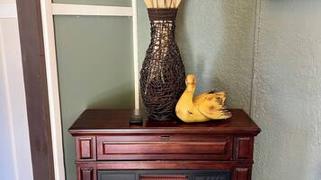 A fireplace with logs burning, a vase with dried plants, and a wall clock.