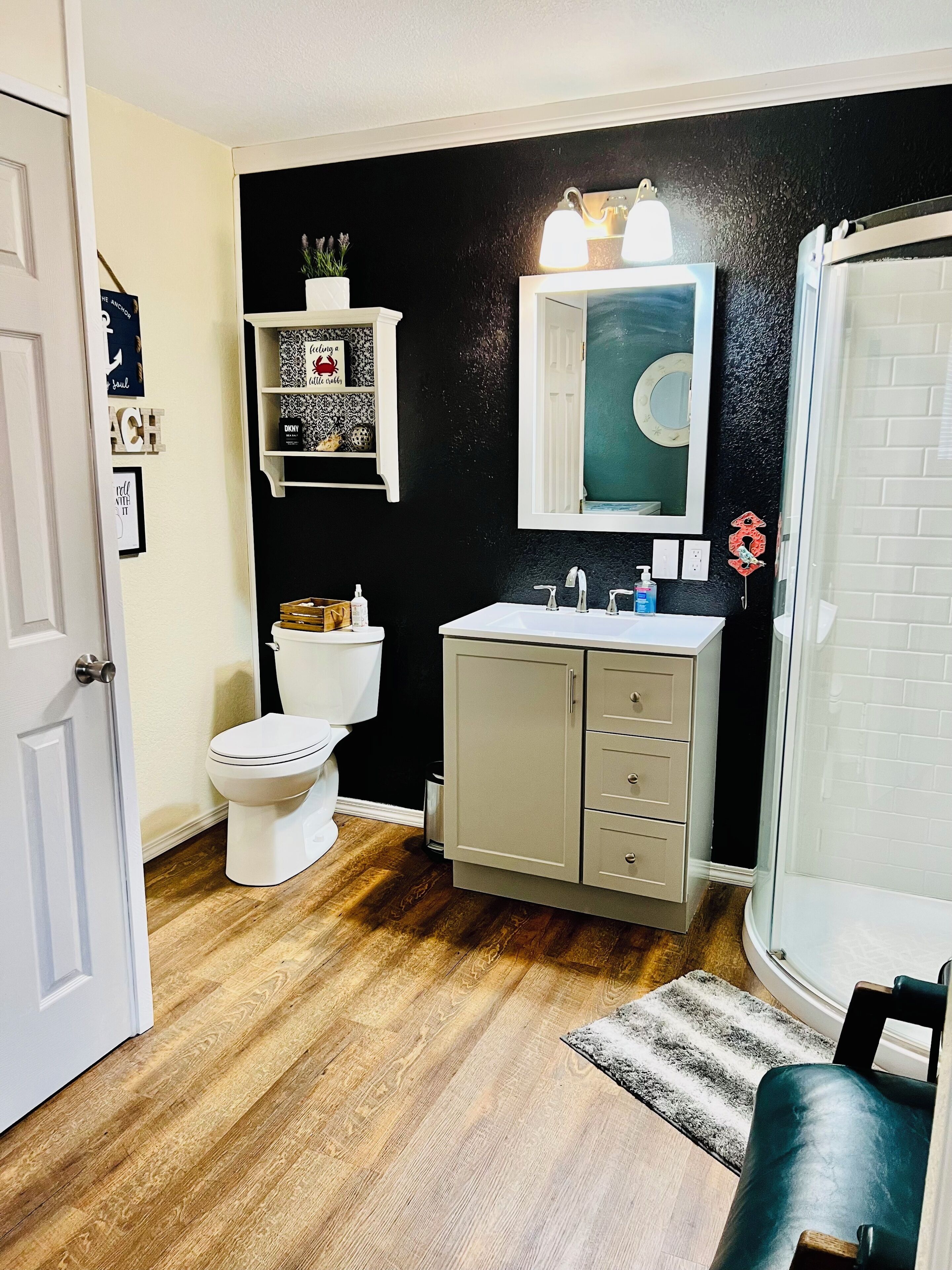 Une salle de bain avec des toilettes blanches, un meuble-lavabo beige, un miroir au-dessus du lavabo et un espace douche.