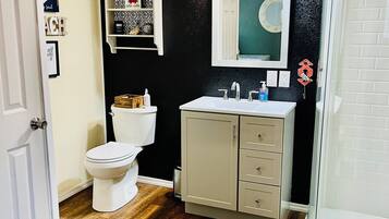 Une salle de bain avec des toilettes blanches, un meuble-lavabo beige, un miroir au-dessus du lavabo et un espace douche.