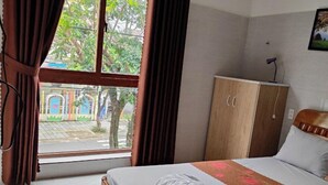 Une chambre d’hôtel avec un lit, une armoire, une fenêtre avec des rideaux et un paillasson.