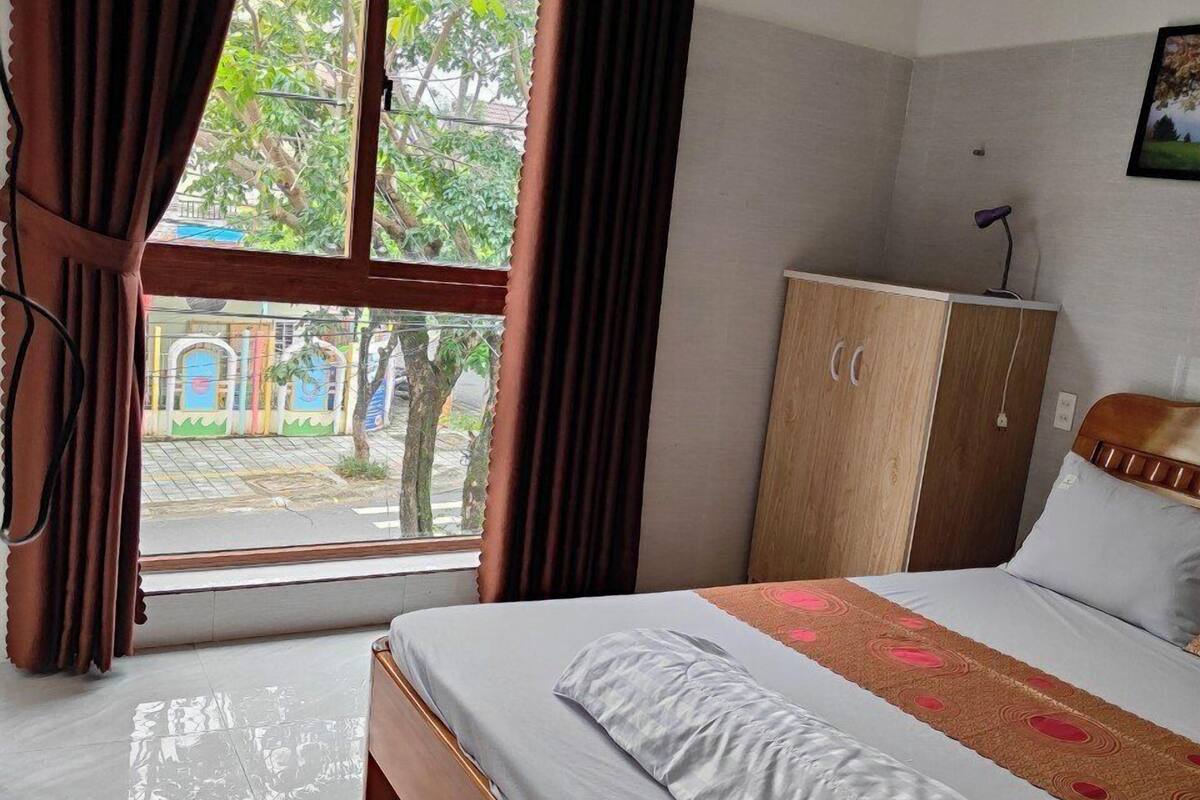 Una habitación de hotel con cama, armario, ventana con cortinas y una alfombra de bienvenida.