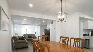 Un comedor con una mesa y sillas de madera, un televisor y una cocina al fondo.