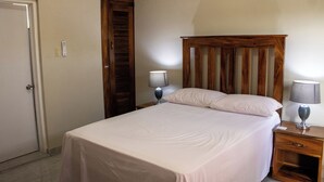 Un lit bien fait dans une chambre dotée d’une tête de lit en bois, de deux lampes de chevet et d’une table de chevet en bois avec un tiroir.