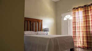 Une chambre à coucher avec un lit, une table de chevet, une lampe et une porte avec une fenêtre.