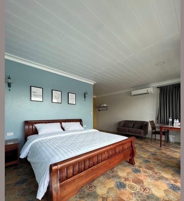 A hotel room with a wooden bed, a desk, a brown sofa, and a patterned floor. - The Lake Khao Yai (Pak Chong)