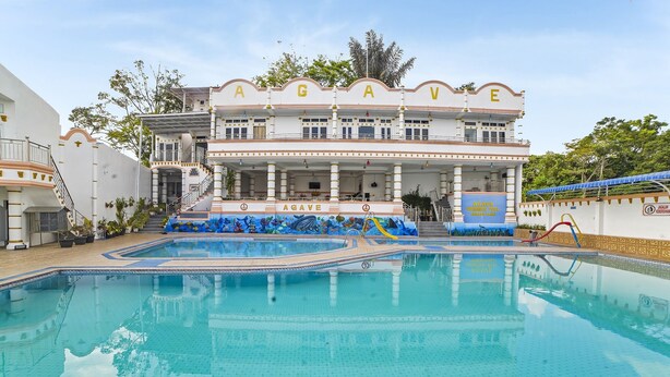 Un edificio grande con una piscina frente a él. El edificio tiene las letras "AGAVE" en la fachada.