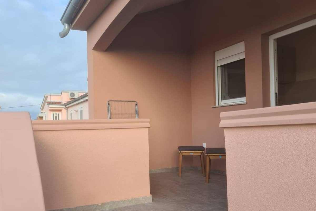 A balcony with a chair and a small table, a window, and a metal railing.