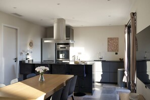 A modern kitchen with a central island, a dining area with a wooden table and chairs, and a large window allowing natural light.