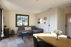 Un salon moderne comprenant un canapé, une table basse, une table à manger et une vue dégagée sur l’extérieur grâce à une grande fenêtre.