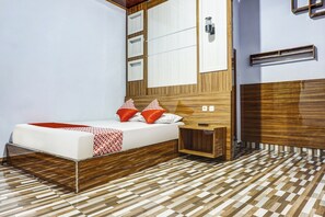 A modern bedroom with a wooden headboard, a bed with red and white bedding, a bedside table, and a patterned floor.