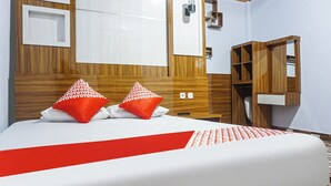 Una habitación de hotel con cabecera de madera, cama con ropa de cama blanca y roja, y un armario de madera.